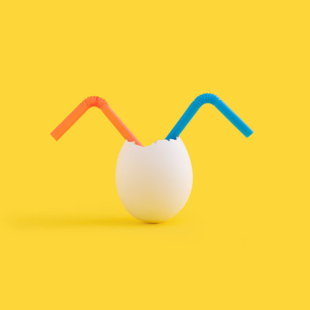 A closeup of two plastic straws in an eggshell against the yellow backgroundの写真素材