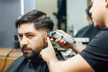 A barber shaving the sides of his client's head in the barbershopの写真素材
