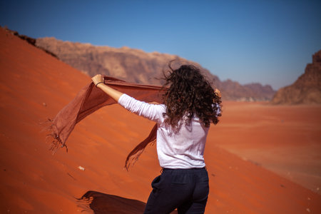 A caucasian female with curly hair posing spreading a cloth to sit on a sunny desertの写真素材