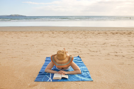 A girl lying on a towel and reading a book on the beach
