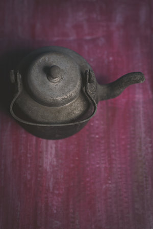 A vertical shot of a rusty iron teapot on a rough red textile background with scratch marksの写真素材