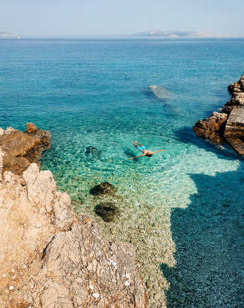 Young tourist relaxing and floating on water surface on beautiful hidden beach with transparent water on Pag island in Croatia.の写真素材