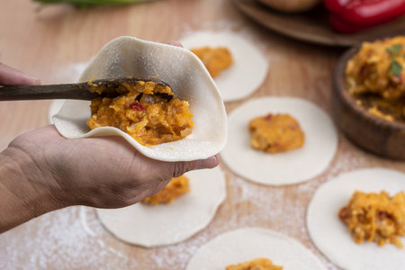 A person making Argentinian empanadas stuffed with vegetables and squash on wooden surfaceの写真素材