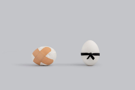 Two decorative eggs the one is covered by medical tapes, and another one has black ribbon on him isolated in white backgroundの写真素材