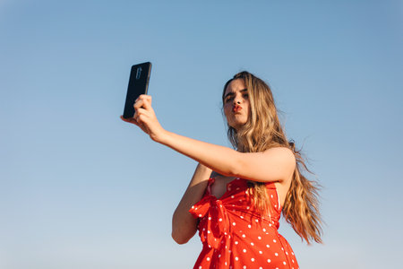 A low angle shot of a young attractive Caucasian female taking a selfie on a fieldの写真素材