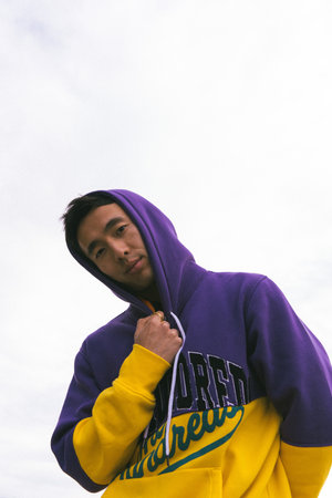 A vertical shot of a sexy Asian male model in a purple and yellow hoodie posing outdoors with clean backgroundの写真素材