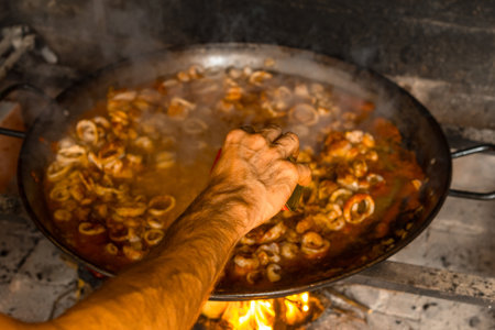 A closeup shot of traditional Valencian paella preparing on wood embers and vegetablesの写真素材
