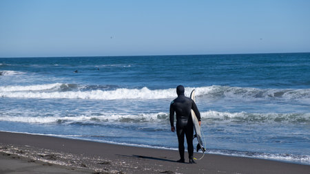 man looking at the sea with his surfboard and wetsuit, a beach in Chile sunny day small waves