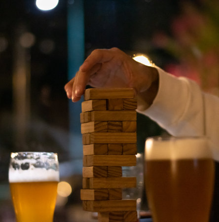 A closeup of glasses of beer and hand playing with wooden blocks on the tableの写真素材