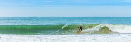 A panoramic view of a surfer sur on the wave in the sea against the blue skyの写真素材