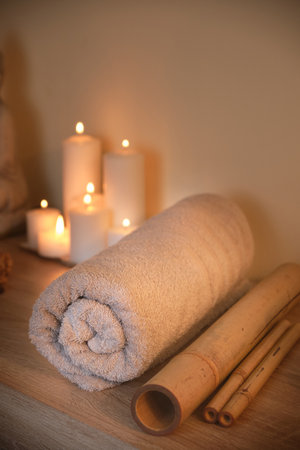 A vertical shot of a rolled spa towel, massage bamboo sticks, and glowing candles in a wellness centerの写真素材