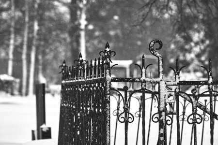 A selective focus shot of a snow-covered metal fence in a graveyardの写真素材