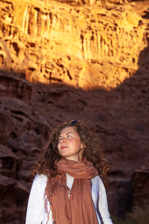 A vertical shot of a beautiful caucasian female with curly hair posing near red sandstone cliffsの写真素材