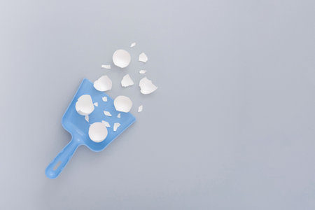 A vertical shot of chicken eggshells in a blue plastic scoop on a white surfaceの写真素材