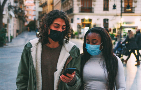 Picture of Interracial Couple With Surgical Masks Looking Mobile Phone at Street.