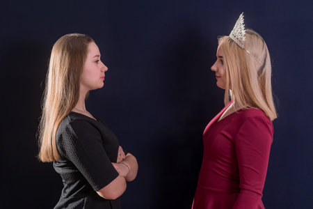 Two young girls, one with a crown on her head, stand opposite each other and look into each other's eyes, dark background.の写真素材