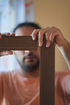 Man shims two pieces of wood at right angles. Assembling a piece of furniture at home. Carpentry sessionの写真素材