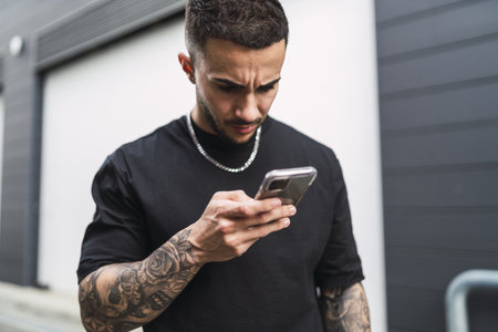 A Spanish man with tattoos looking at his phone with a worried faceの写真素材