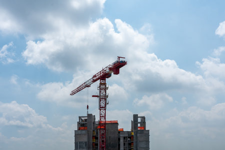Construction crane on top of skyscraper against blue cloudy sky. Horizontal shotの写真素材