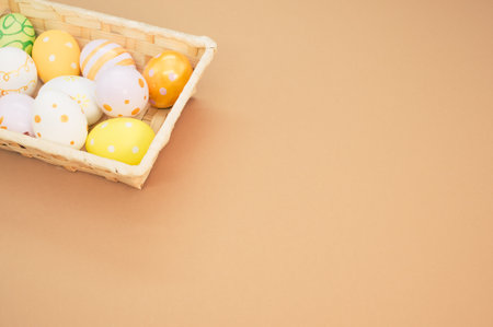 A woven basket with decorated Easter eggs on peach-colored backgroundの写真素材