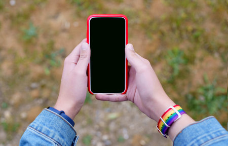 A top view of female hands with a rainbow LGBT bracelet holding a smartphoneの写真素材
