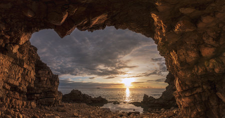 the beautiful seascape through the rocks on the cloudy sky background at sunsetの写真素材