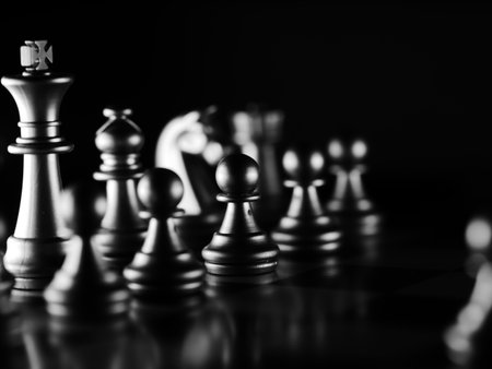 A dramatic grayscale shot of chess figures lit in the darkness