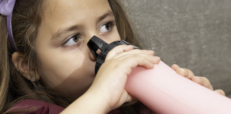 A Latina girl sitting on the sofa at home and drinking from the bottleの写真素材