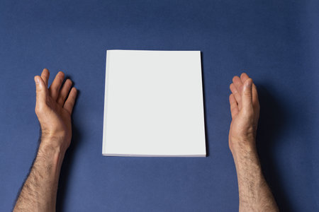 Male hands around a closed book catalog with blank cover on blue backgroundの写真素材