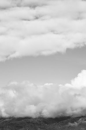 A grayscale shot of hills covered in the fog under a cloudy sky in the countryside