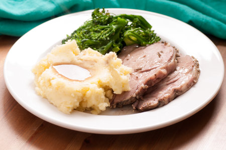 roasted leg of lamb with mashed potato, gravy and greensの写真素材
