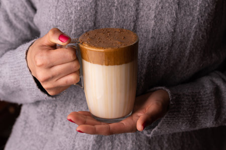 A woman in wool sweater holding a glass of creamy dalgona coffee sprinkled with chocolateの写真素材