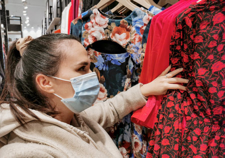 A shallow focus of Croatian woman wearing a face mask while choosing a dress in a storeの写真素材