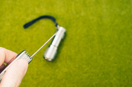 A selective focus shot of a hand holding a knife with a flashlight on the grass in the backgroundの写真素材