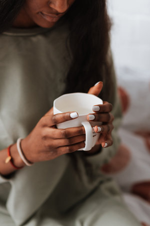 A young African female holding a white ceramic mug while sitting on the bedの写真素材
