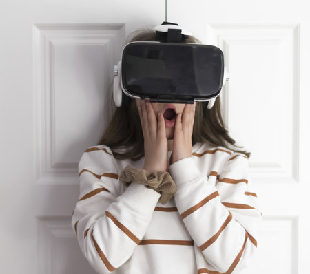 The picture shows a medium shot of a little girl wearing virtual reality goggles with her hands on...