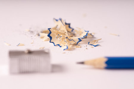 A selective focus shot of pencil shavings with a blue pencil and metal sharpener in the foregroundの写真素材