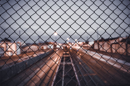 A high angle shot of a cityscape and rail tracks seen through metal mesh fenceの写真素材