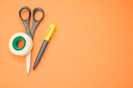 A closeup shot of scissors adhesive tape and a utility knife on an orange backgroundの写真素材
