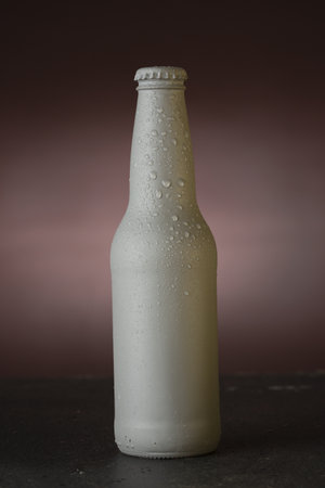 A vertical shot of a white soda/beer bottle with water drops and a black backdropの写真素材