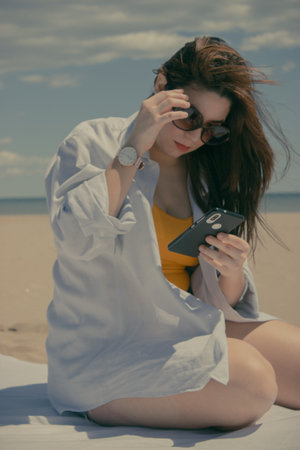 A young Caucasian girl with sunglasses looking at her phone to share her day at the beach on social mediaの写真素材