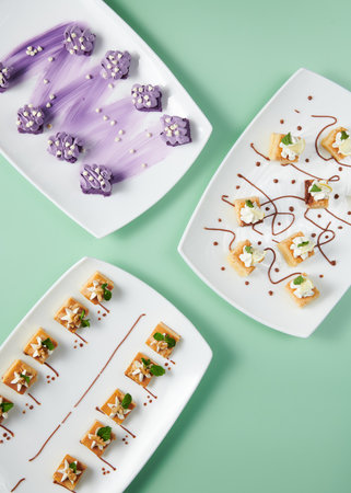 A vertical top view of small cakes served on decorated plates on a minty backgroundの写真素材