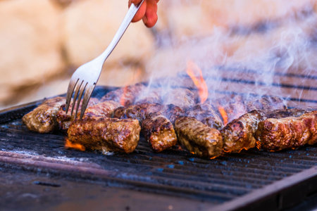 A closeup of hand preparing meat rolls called mici or mititei on barbecue with rising smokeの写真素材