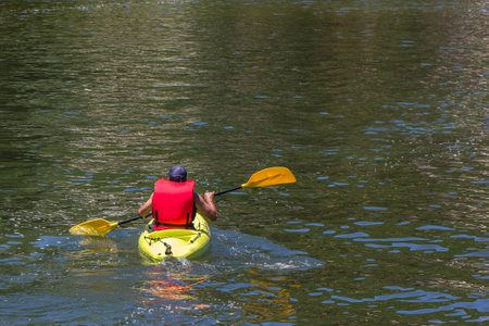 A guy in a boat and a swimming jacket paddling on a lakeの写真素材