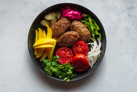 A top view of meat cutlets and vegetables on a black plate on a white surfaceの写真素材