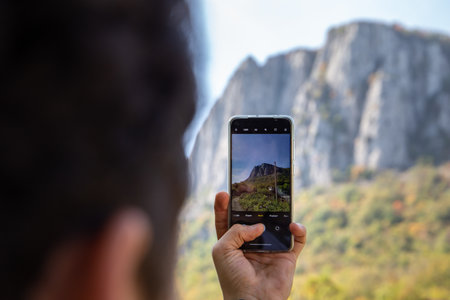 A selective focus shot of a person taking a pic of a cliff with their mobile phoneの写真素材