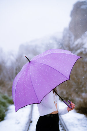 A vertical shot of an unrecognizable girl wearing a hat and holding a purple umbrella on a snowy dayの写真素材