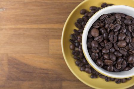 coffee cup top view, yellow ceramic cup and saucer filled with coffee beans on a wooden surface, with space to write to the left, horizontal photoの写真素材