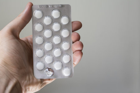 A closeup of a person holding a pack of white tablets on a gray background