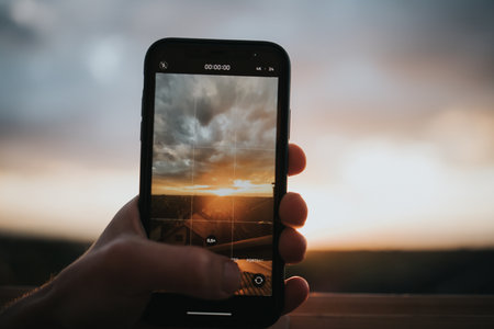 A closeup shot of a person's hand photographing the sunset with the phoneの写真素材
